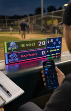 FieldFire Standard three-panel LED matrix scoreboard at a community baseball scorer's table with FieldFire Mobile Manual Control on a phone.
